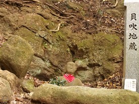 [10]貝吹地蔵。右脇の説明文には「新田義貞の軍に敗れ敗走する北条氏の部下たちを助けるため貝を吹き鳴らした」とある。下半身は土の中？（天園ハイキングコース）